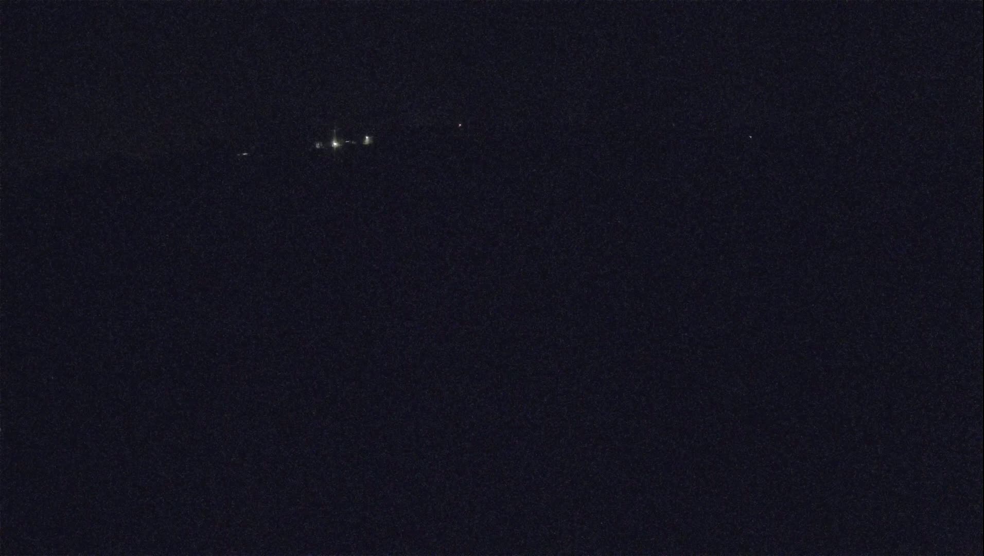 A dark, nighttime scene shows a few faint lights in the distance.
