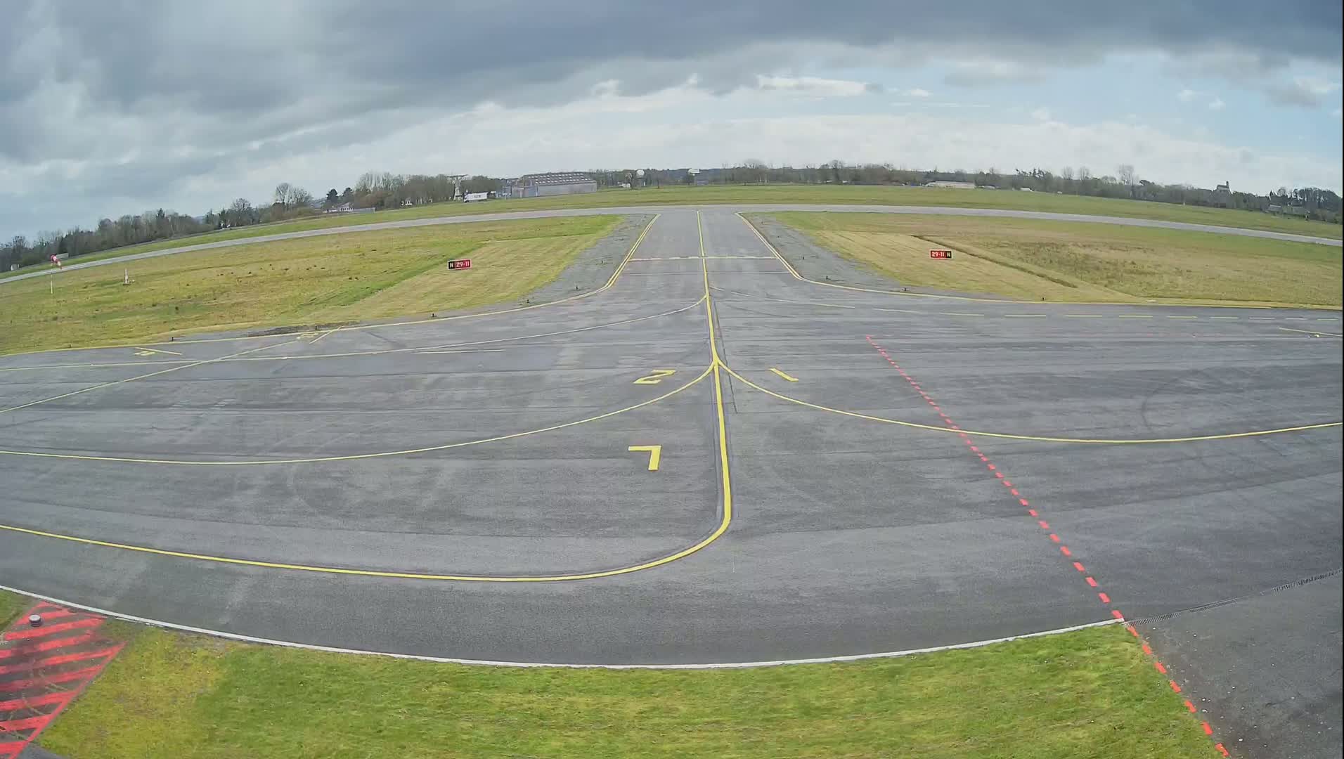 An airfield with a runway and taxiway is shown under a cloudy sky.