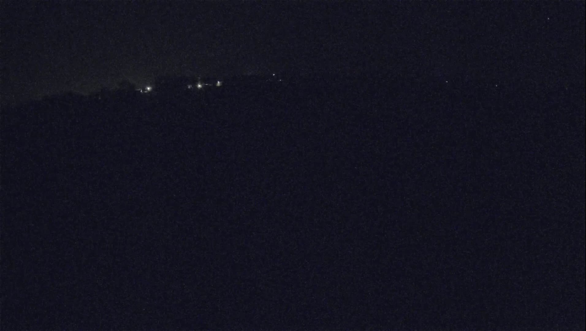 A dark, nighttime view shows a distant line of faint lights against a dark landscape under a clear, night sky.