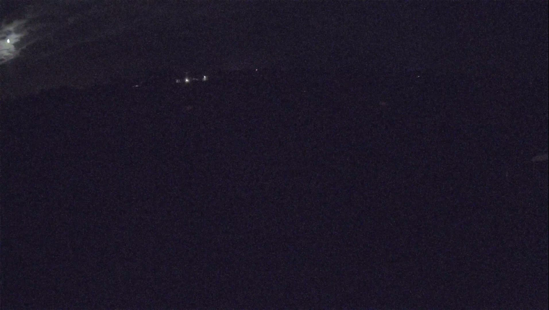 A nighttime long shot shows a dark landscape under a partly cloudy moonlit sky, with a few faint lights visible in the distance.