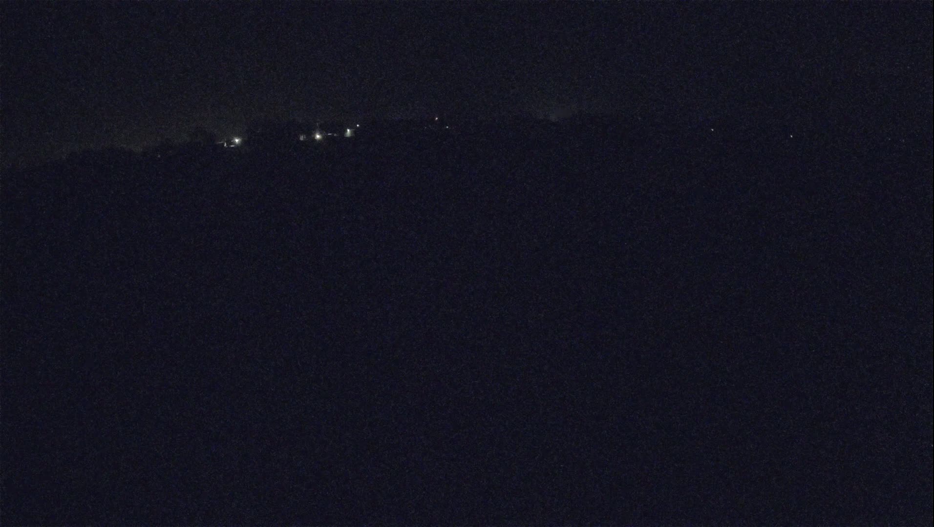 A dark, nighttime landscape shows a distant line of faint lights against a black sky.