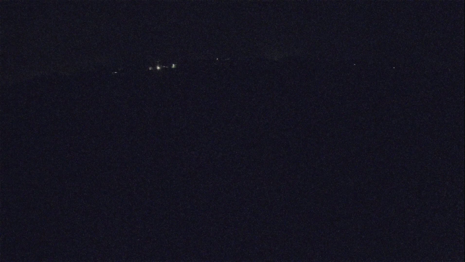 A dark, nighttime scene shows a few faint lights in the distance.