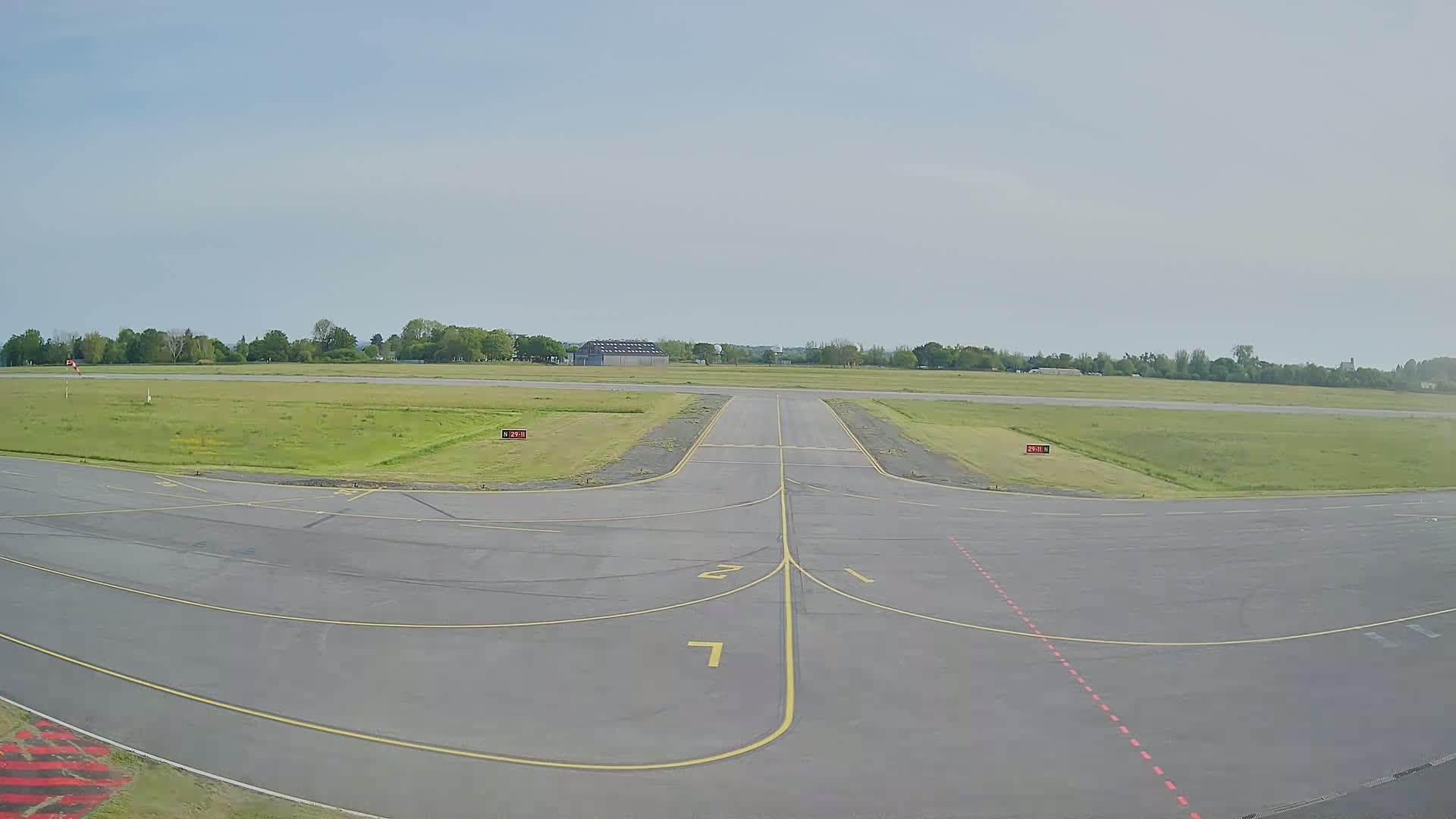 A runway at a small airport on a partly cloudy day, with grassy areas on either side.