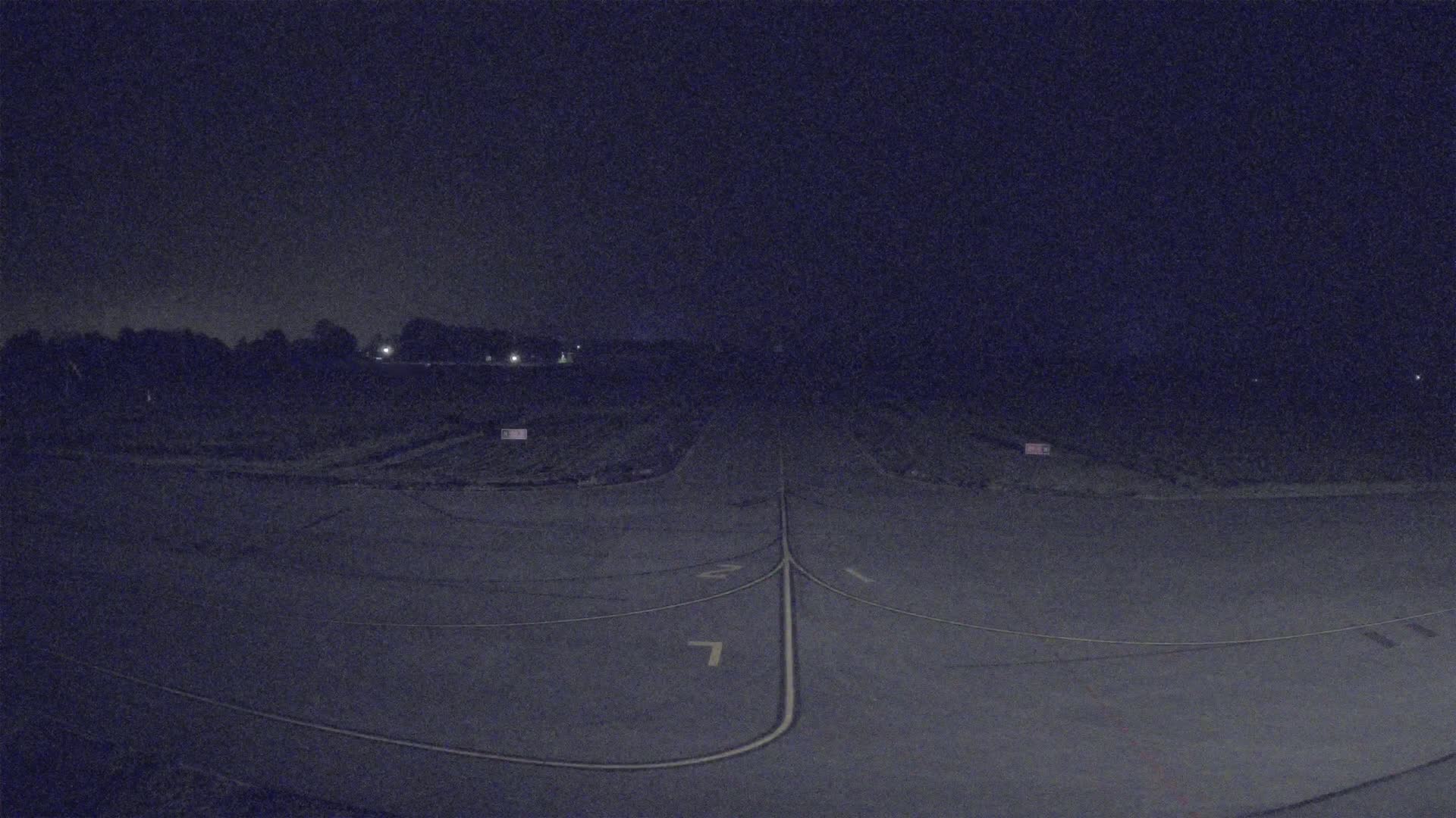 A dark, nighttime view of an empty airport runway with faint lighting in the distance.