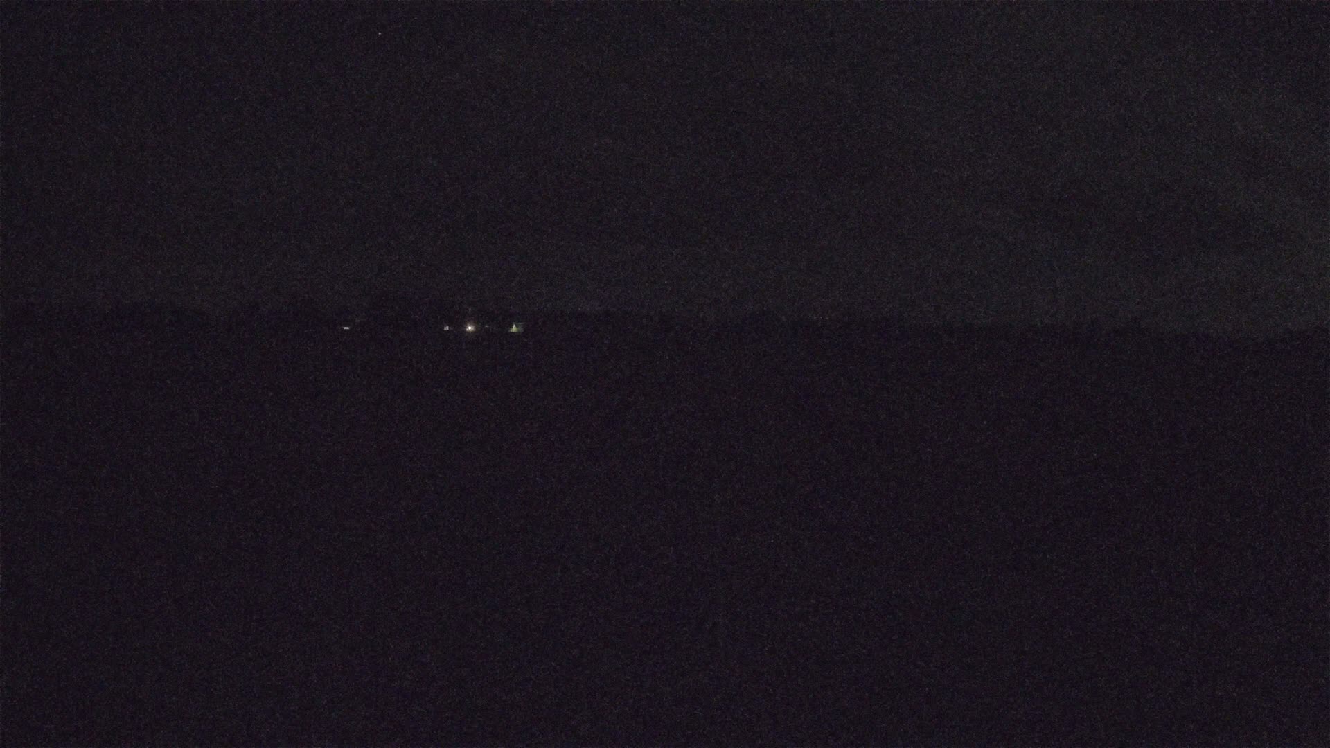 A dark, nighttime scene shows a few faint lights on a distant horizon.