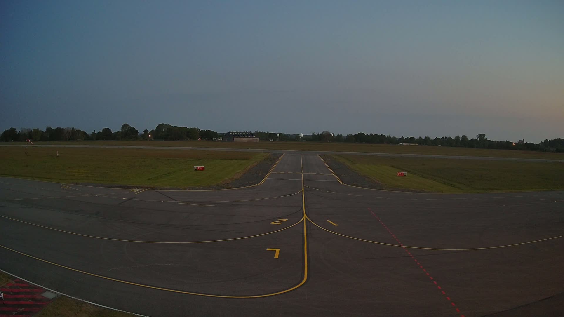 An empty airport runway and taxiway are visible under a twilight sky.