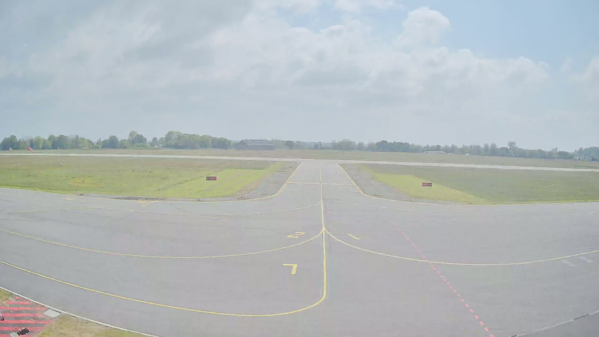 A paved airport runway and taxiway are visible under a partly cloudy sky.