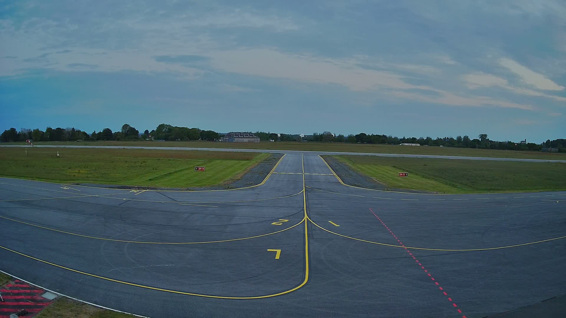 A runway at a small airport under a partly cloudy sky, with grassy fields surrounding the tarmac.