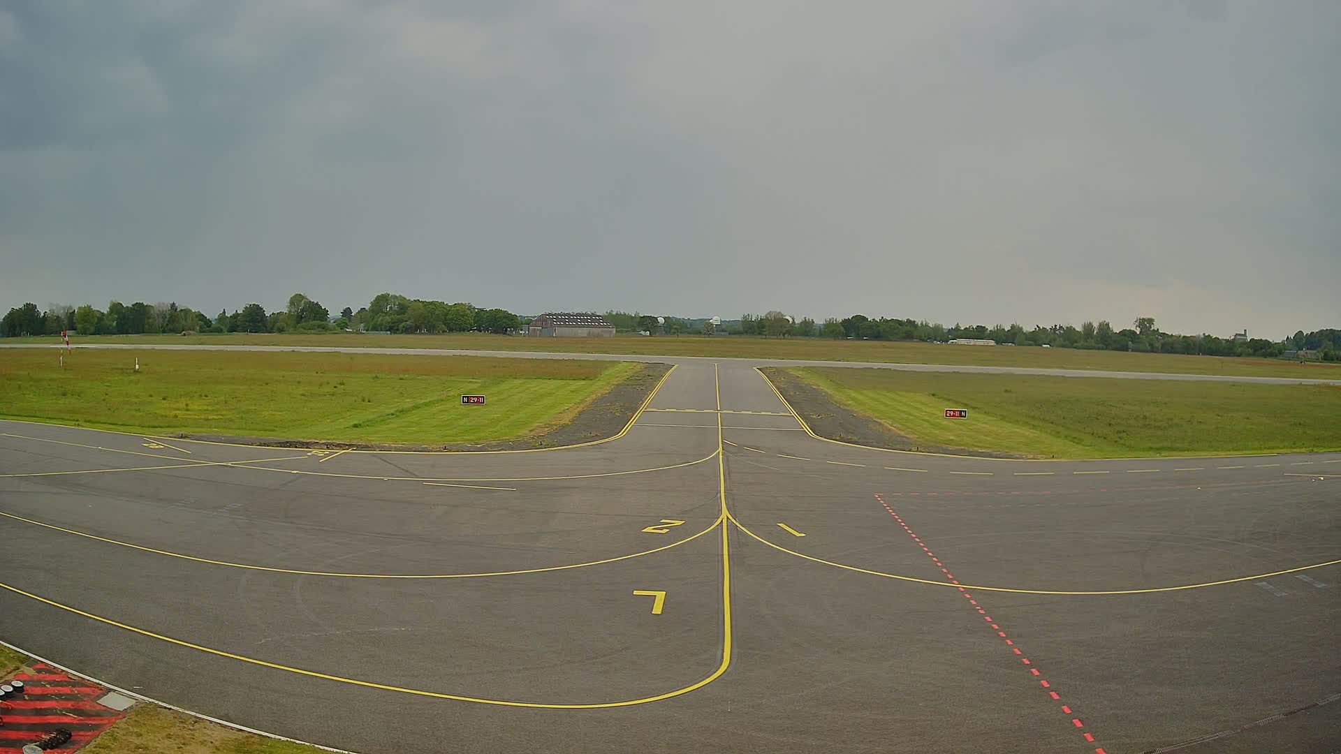 An overcast sky hangs over a small airport runway with grassy areas on either side.