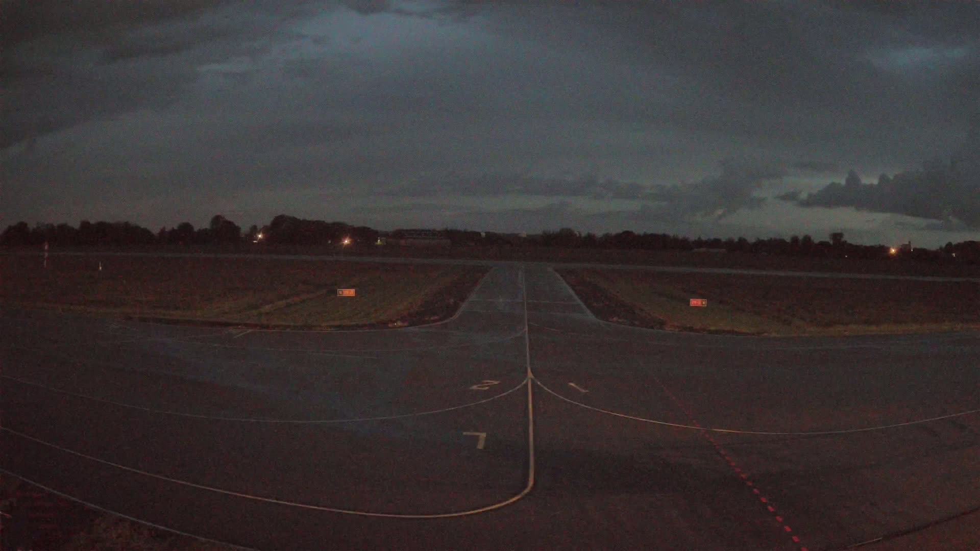 A dark, overcast sky looms over a deserted airfield with a runway and taxiway markings faintly visible under dim lighting.