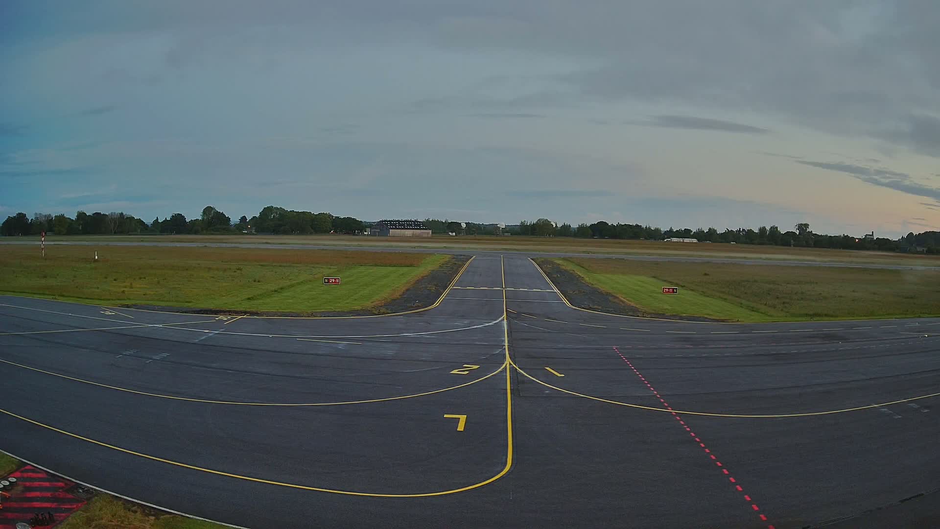 An airport runway with yellow lines and a grassy area under an overcast sky.