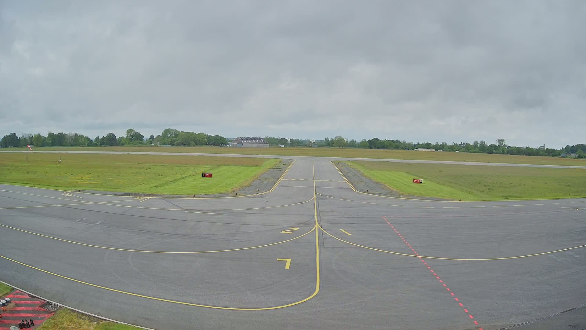 An airport runway leads to a grassy field under an overcast sky.
