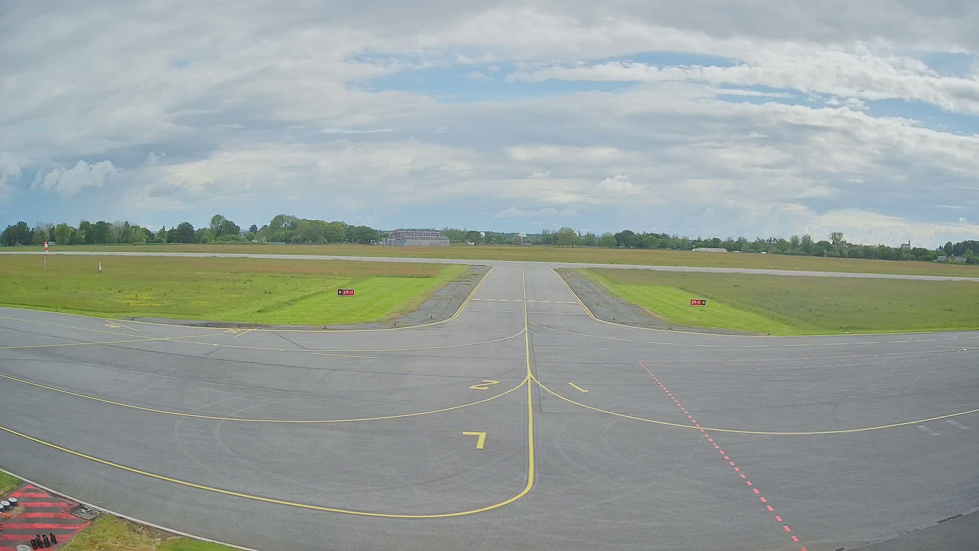 An airport runway with grassy areas on either side under a partly cloudy sky.