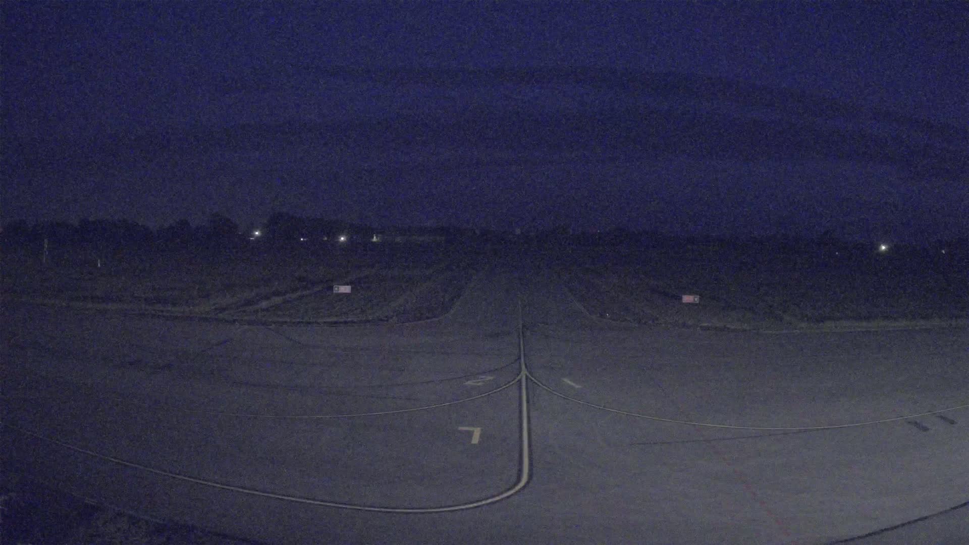 An empty airport runway is visible at night under a dark, overcast sky.
