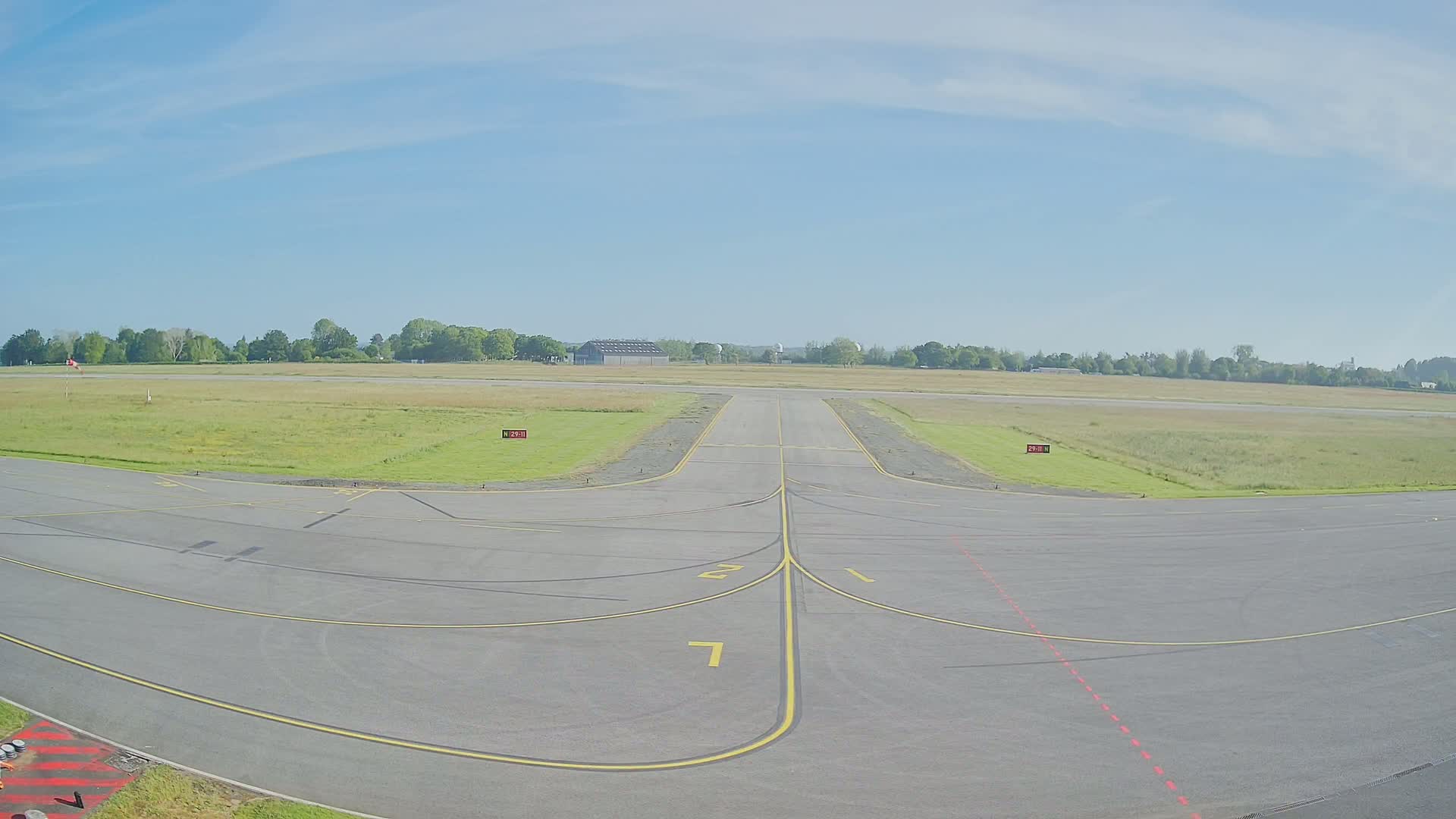 A tarmac airport runway leads to a grassy field under a clear blue sky.