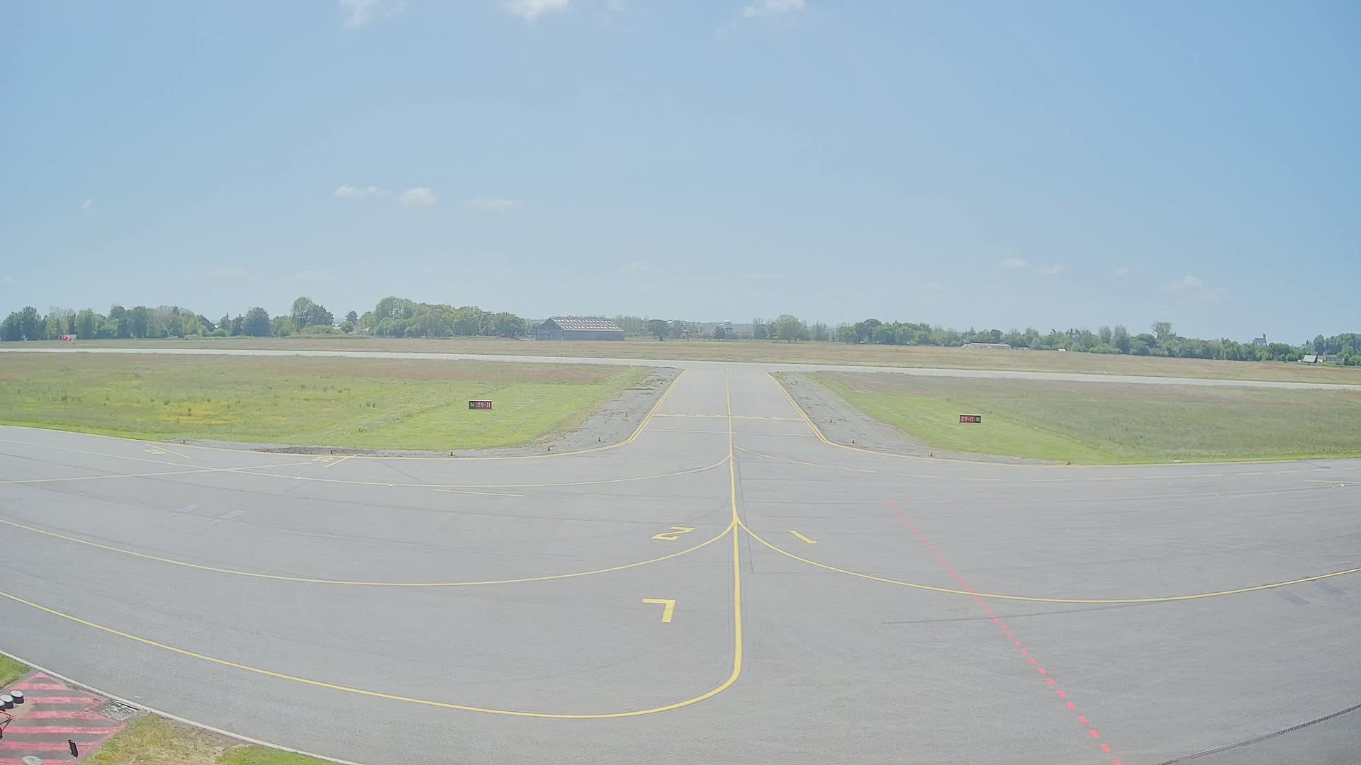 A runway at a small airport on a partly sunny day, with grassy fields surrounding the tarmac.