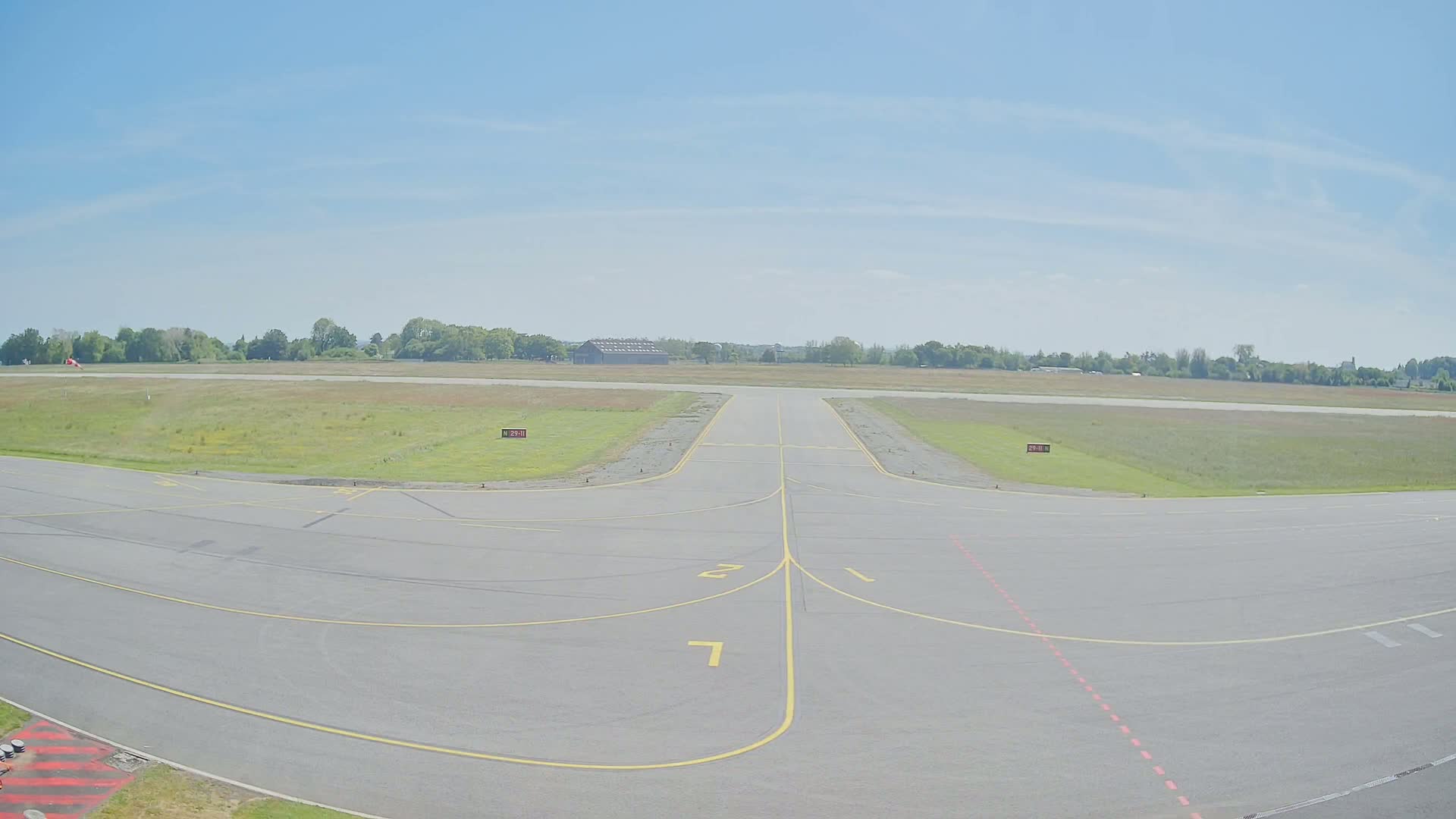 A paved airport runway and taxiway extend toward a grassy field under a clear, bright sky.