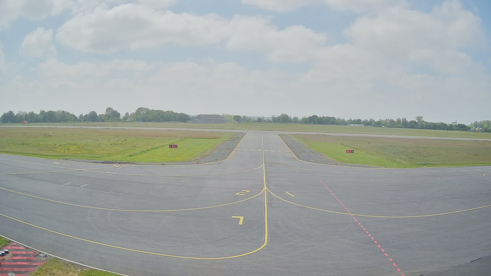 A runway at a small airport on an overcast day with green fields surrounding it.