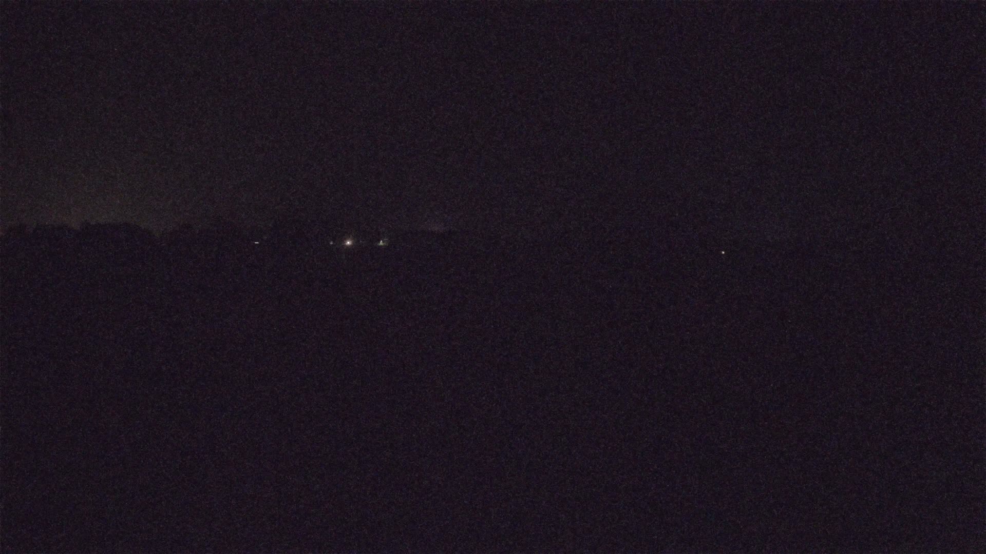 A dark, nighttime landscape is visible, showing a few faint lights in the distance.