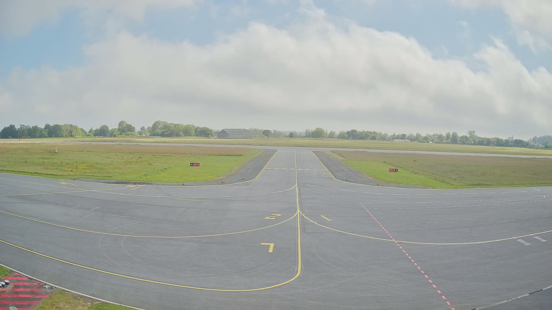 A runway at a small airport on a partly cloudy day, with grassy fields surrounding the tarmac.