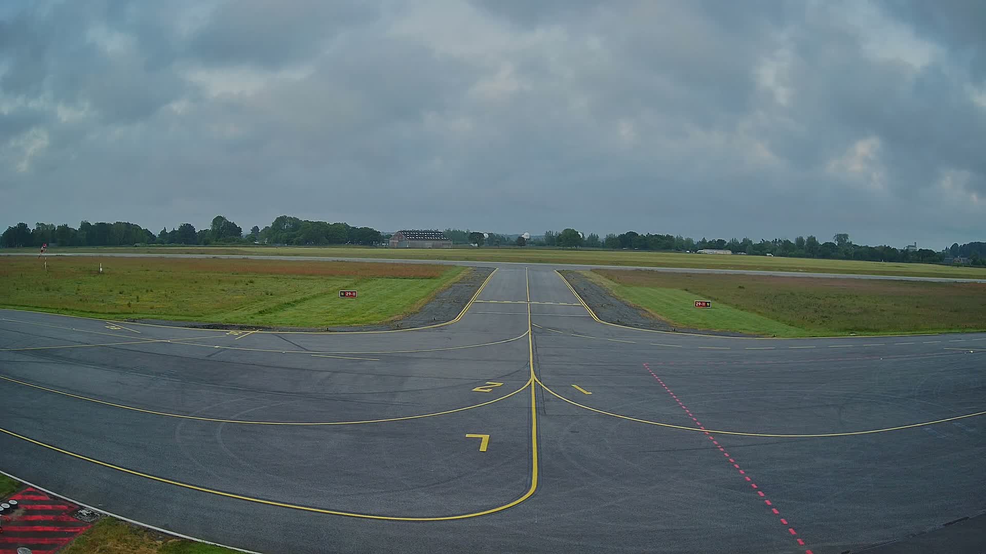 An airport tarmac with yellow lines marking taxiways under an overcast sky.