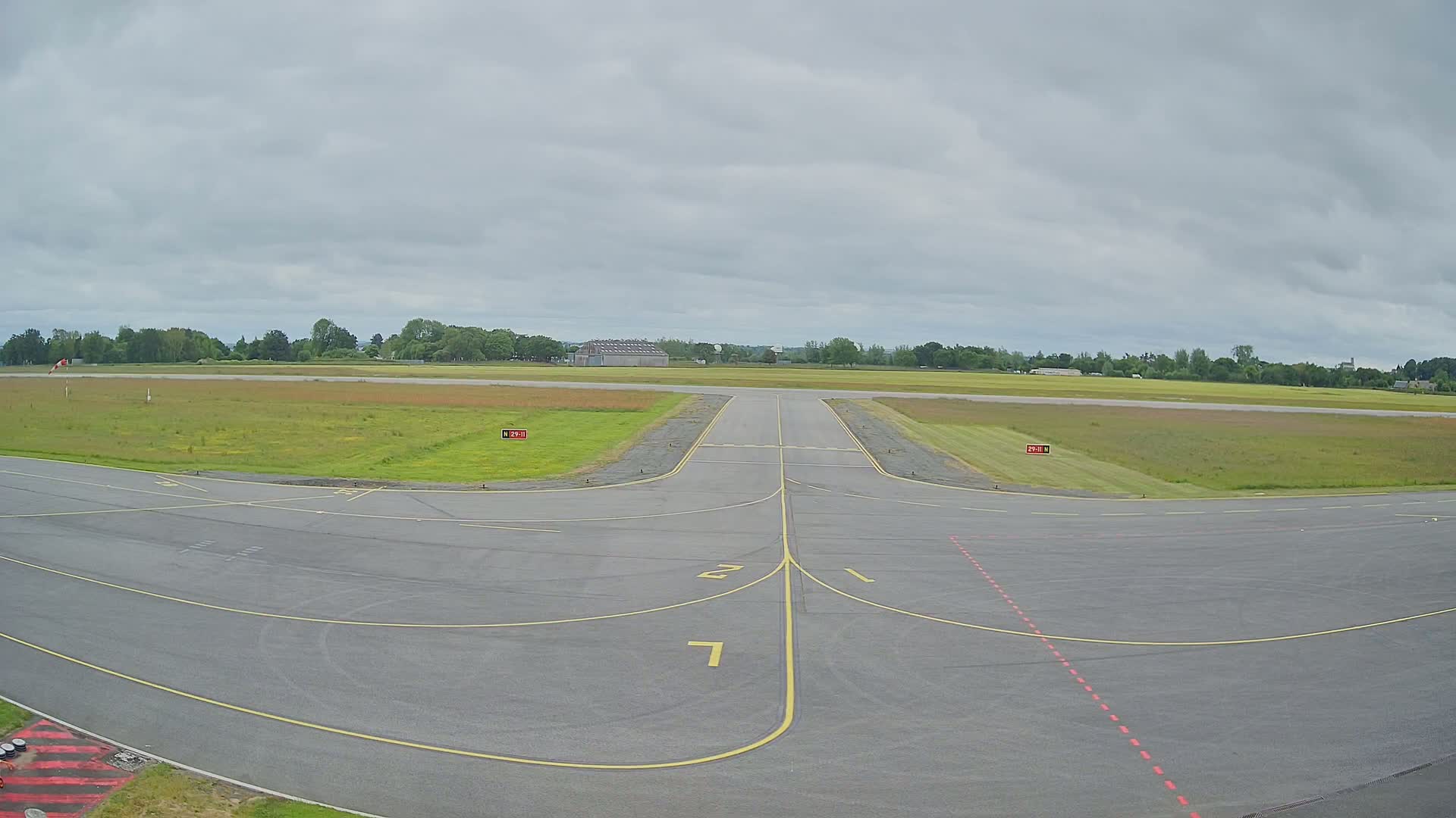 An airport runway with grassy fields on either side under an overcast sky.