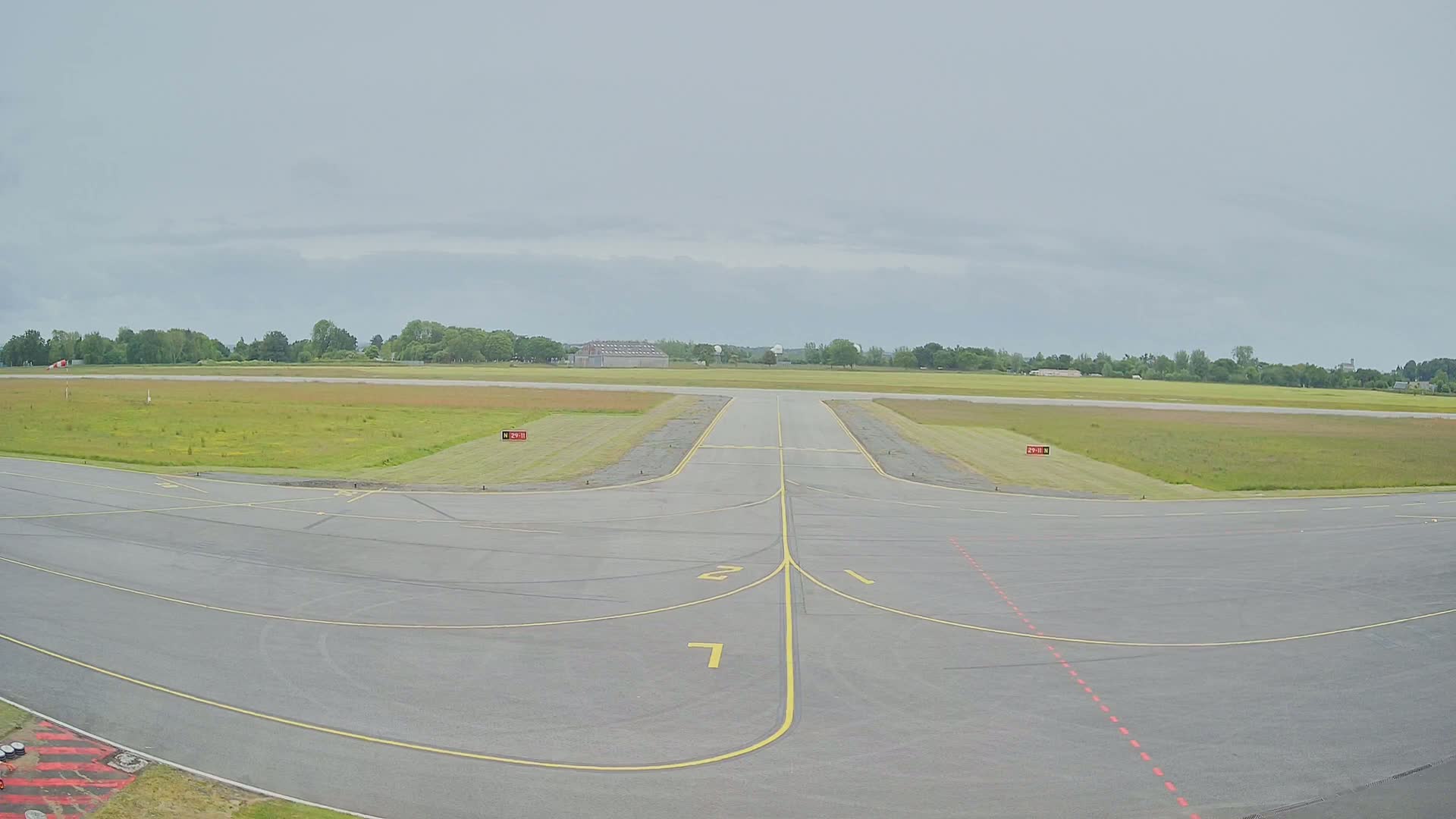 A runway at a small airport on an overcast day, with grassy fields surrounding the tarmac.