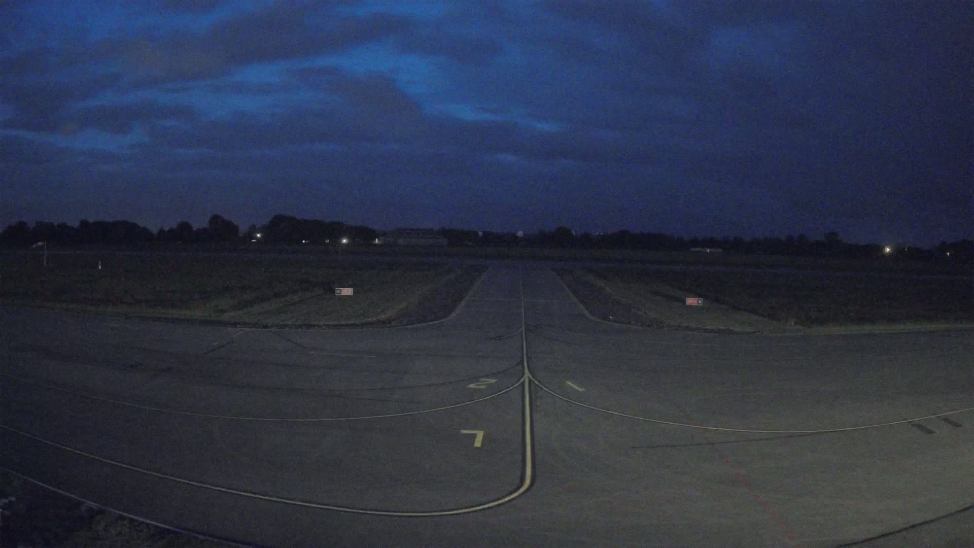 An empty tarmac runway at night under a dark blue, cloudy sky.
