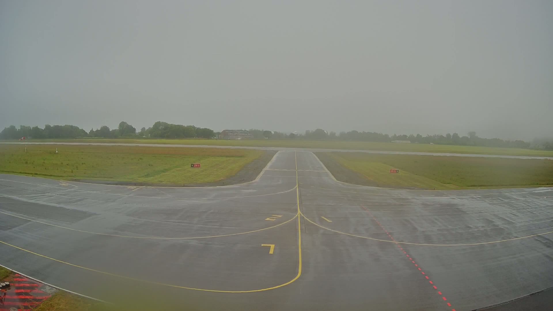 A wet airport runway is visible, under an overcast sky.