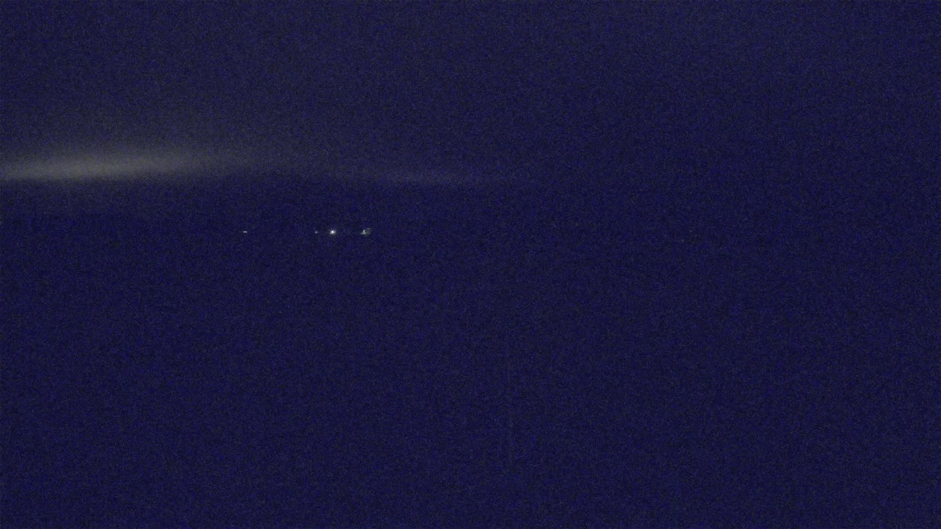 A dark blue night sky shows a faint, horizontal light streak and a few distant, small lights.