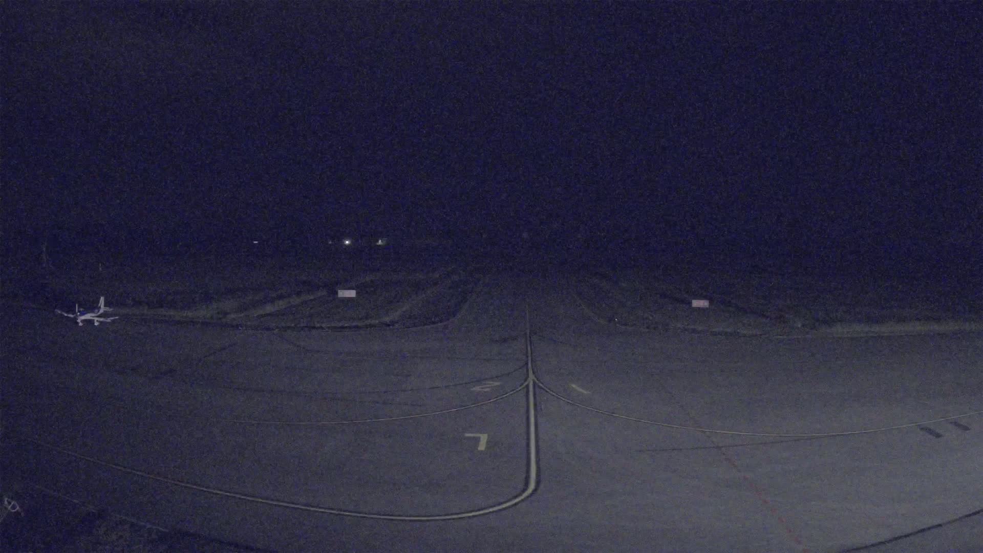A small airplane sits on a dark tarmac at night, with faint lights visible in the distance.