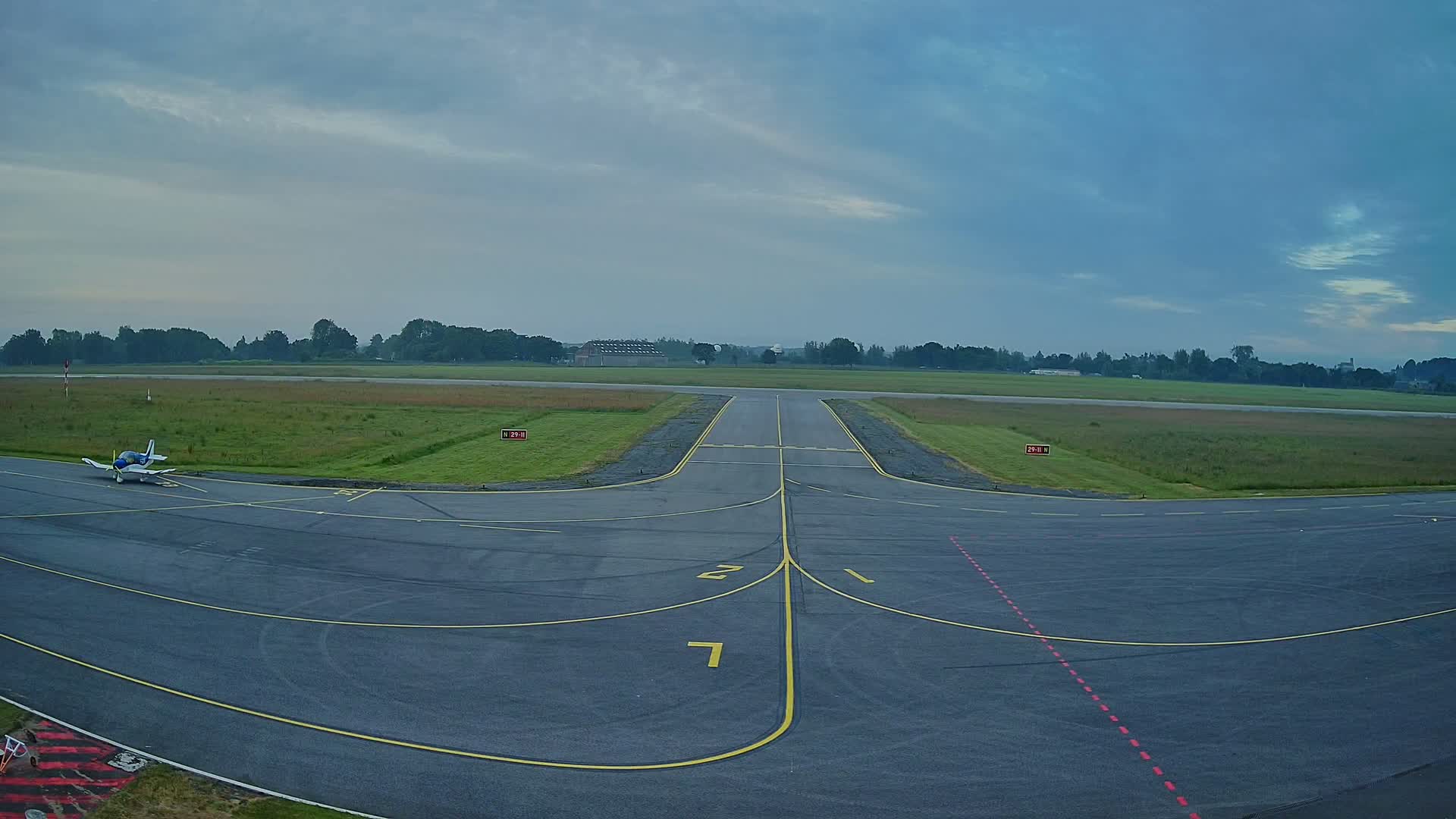 A small airplane sits on a tarmac at an airfield under a mostly cloudy sky.