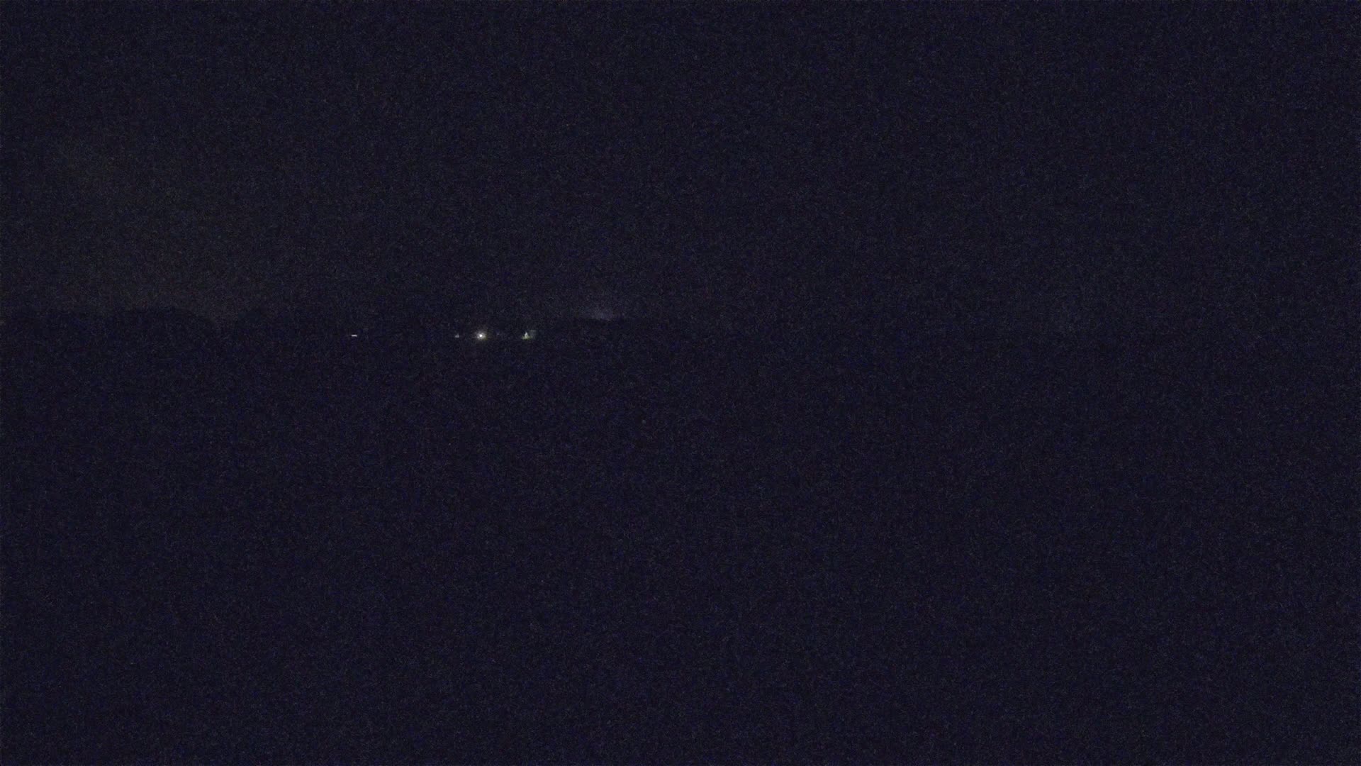 A dark, nighttime scene shows a few faint lights in the distance.