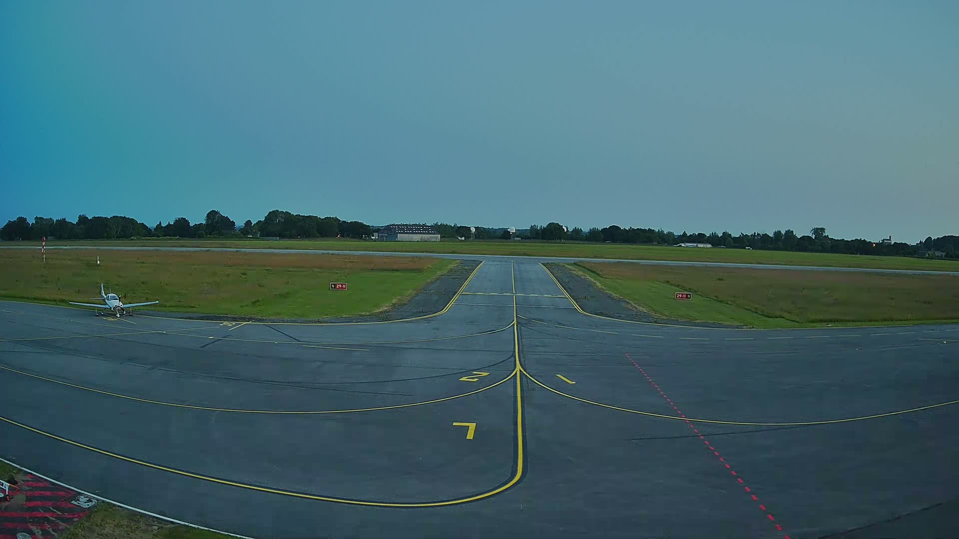 A small airplane sits on a tarmac at an airfield under a clear, dusky sky.
