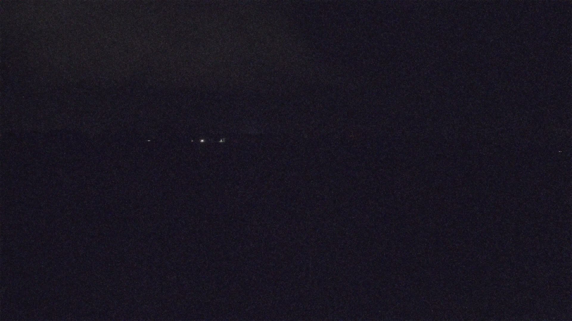A dark, nighttime scene shows a few small, distant lights in the center of the frame.