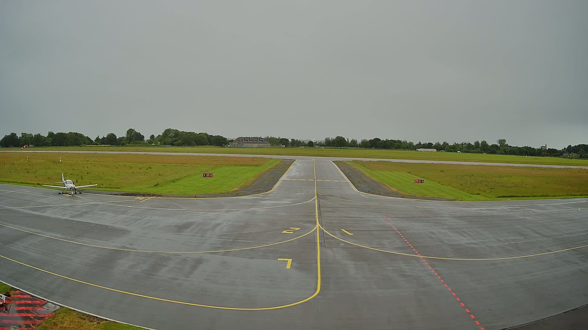 A small airplane sits on a wet tarmac at an airfield under an overcast sky.