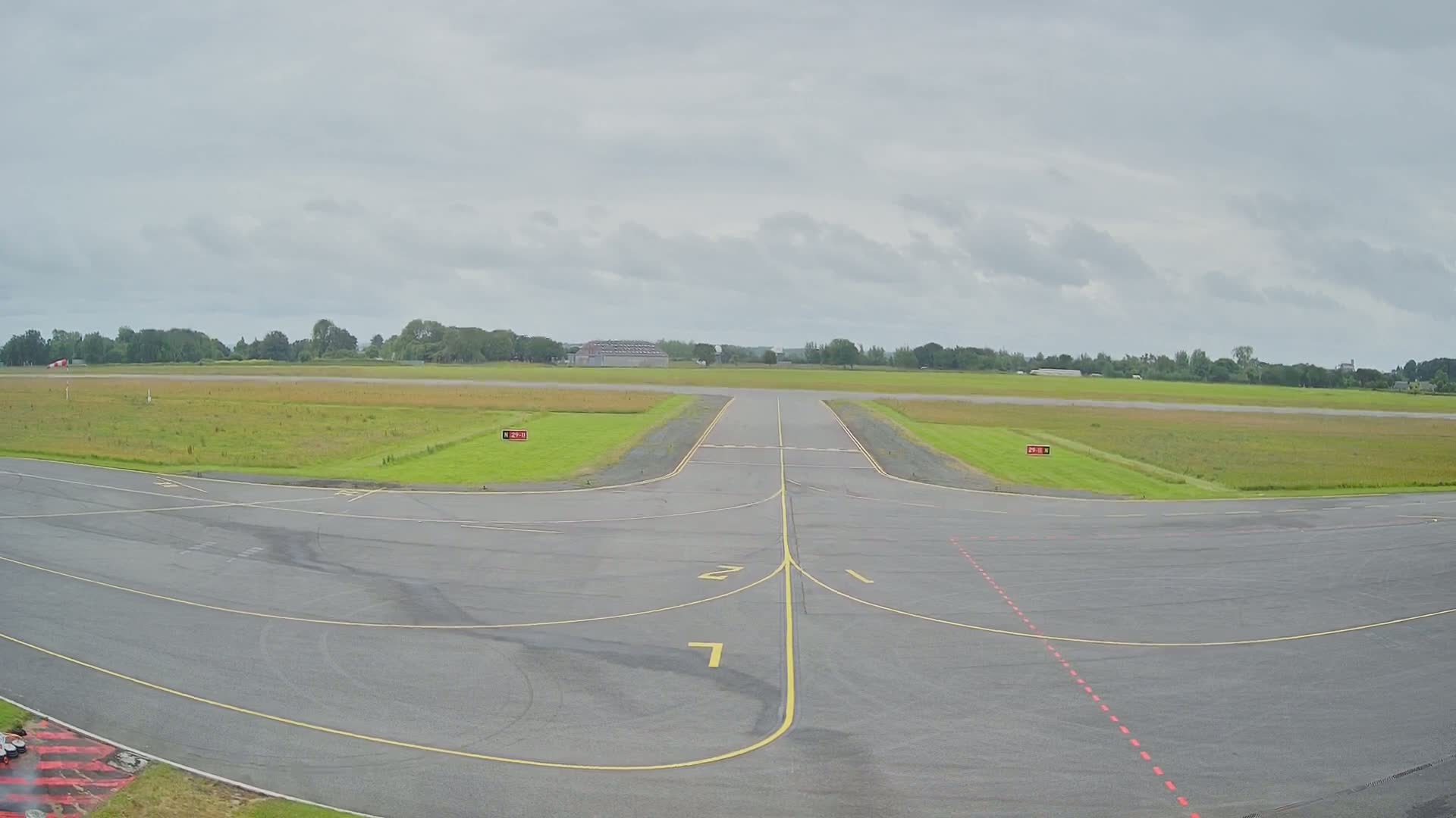 A runway at a small airport on an overcast day extends toward a grassy field bordered by trees.