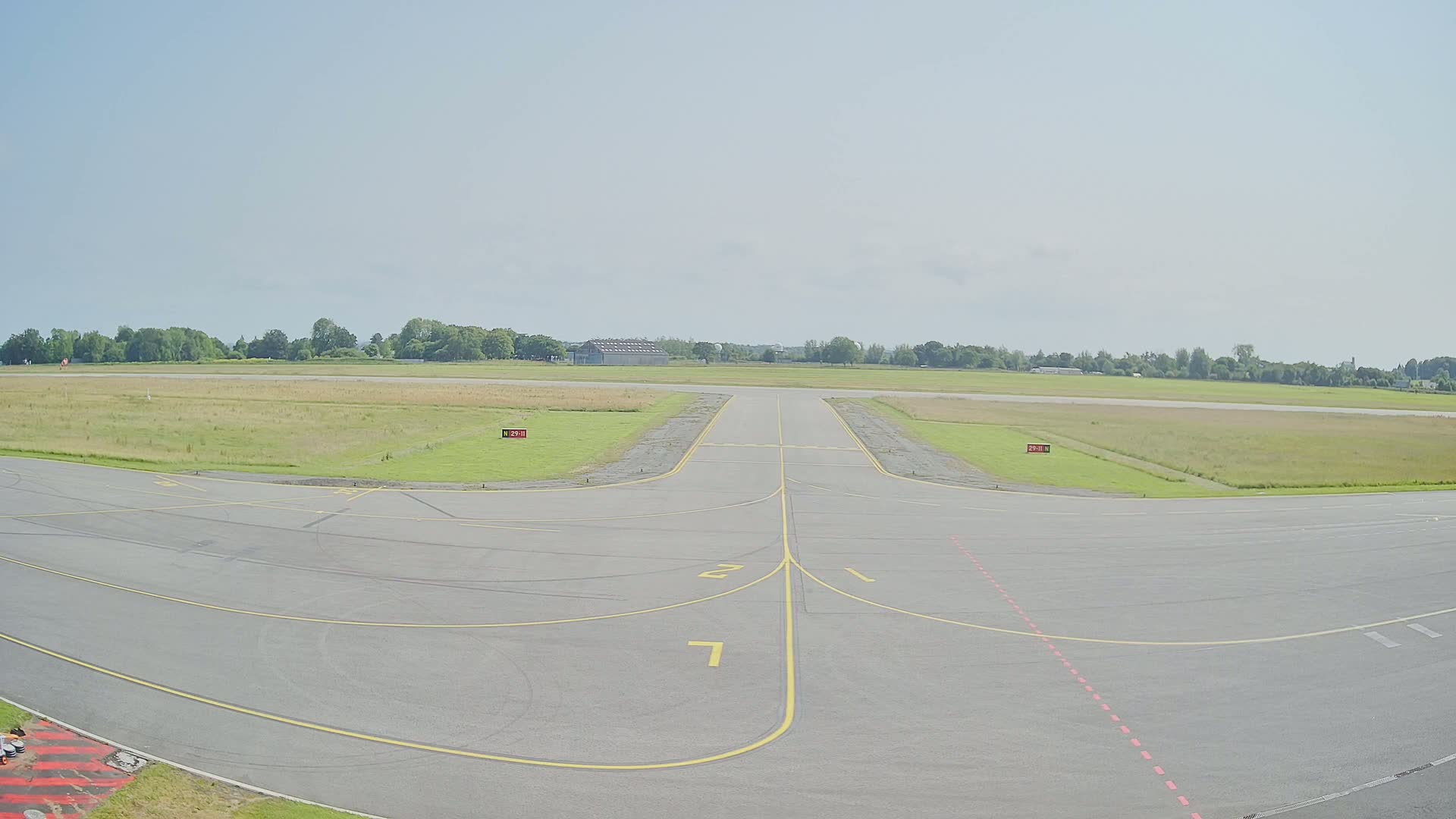 A paved runway at an airfield stretches toward a grassy field under a clear sky.