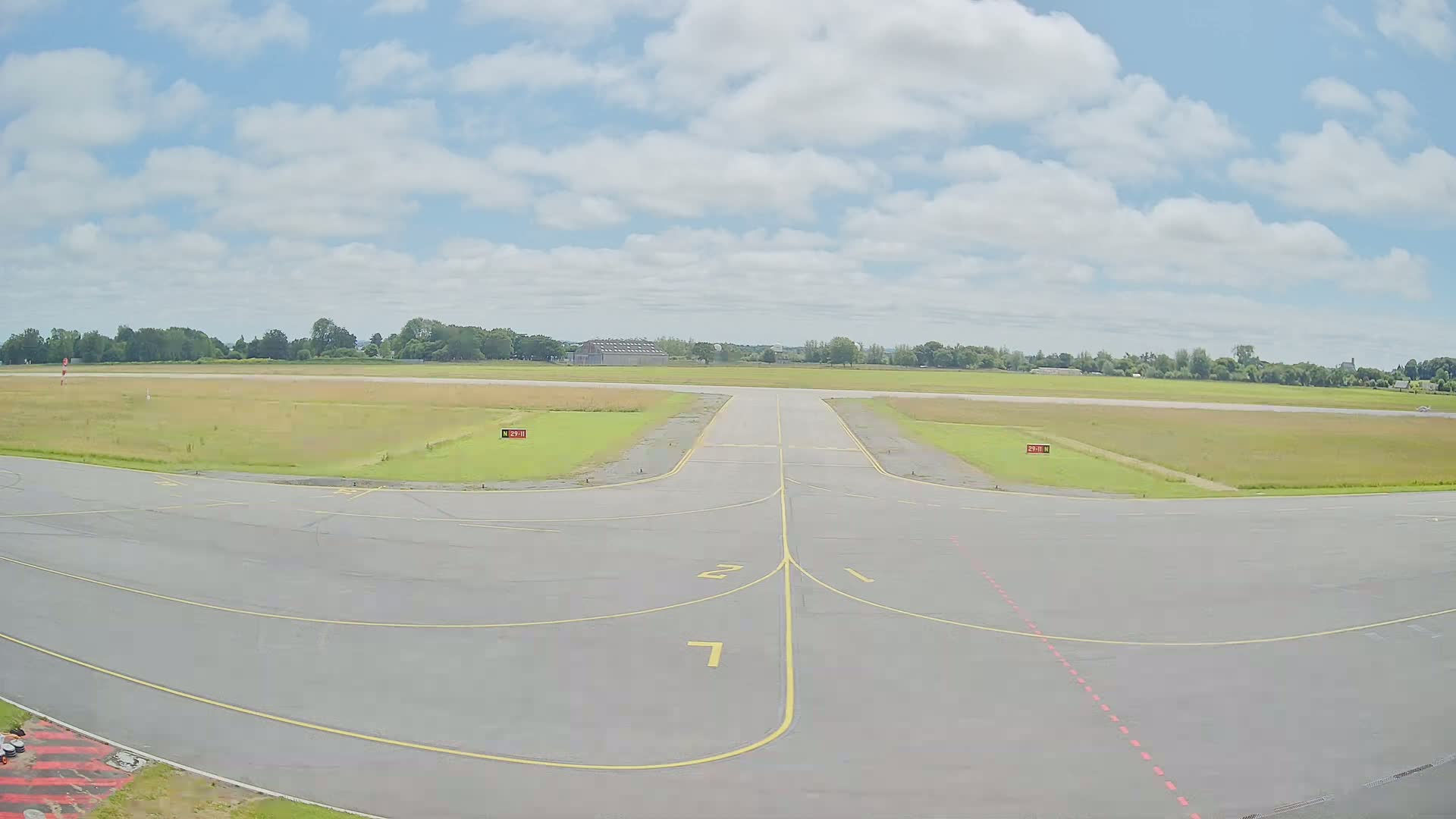 An airport runway and taxiway under a partly cloudy sky.