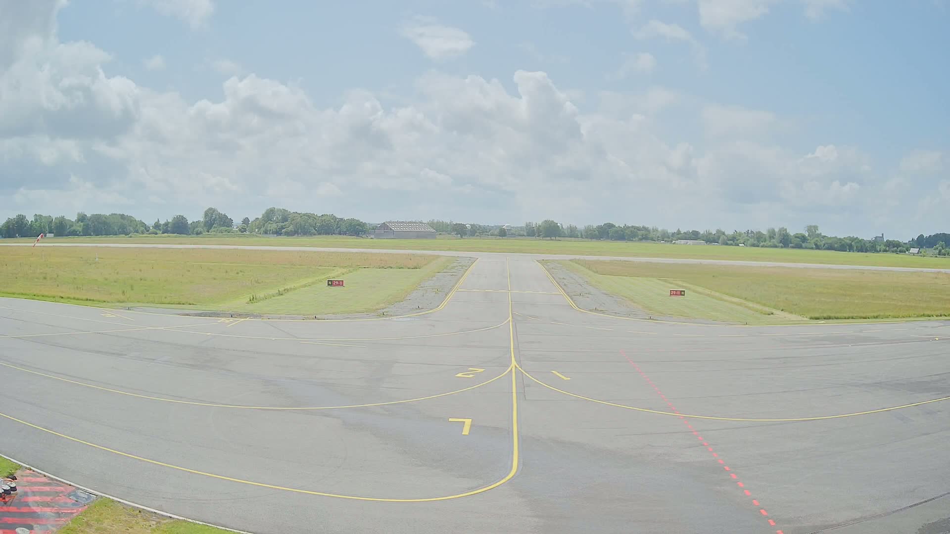 A runway at a small airport on a partly cloudy day, with green fields bordering the tarmac.