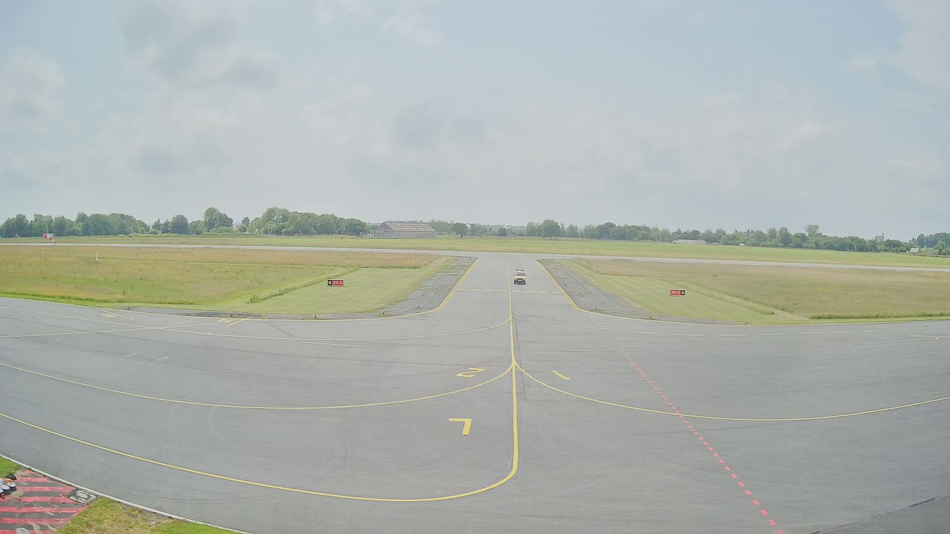 A vehicle drives down a runway on a mostly sunny day with light clouds.