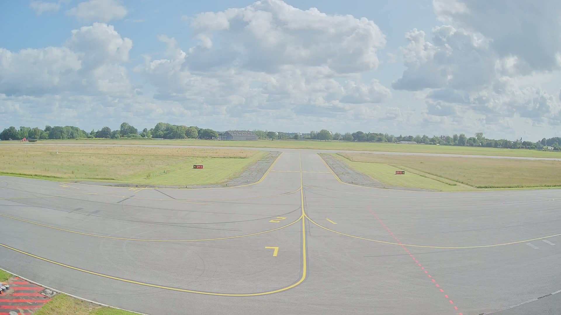A paved airport runway and taxiway under a partly cloudy sky.