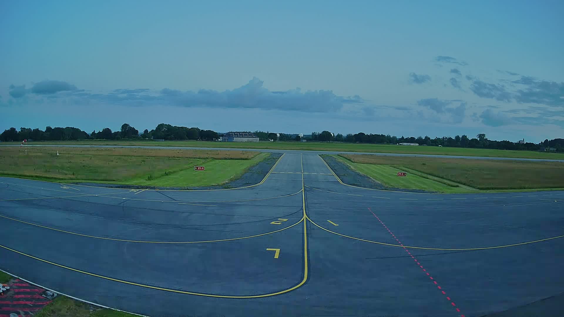 A paved airport runway and taxiway under a partly cloudy sky.