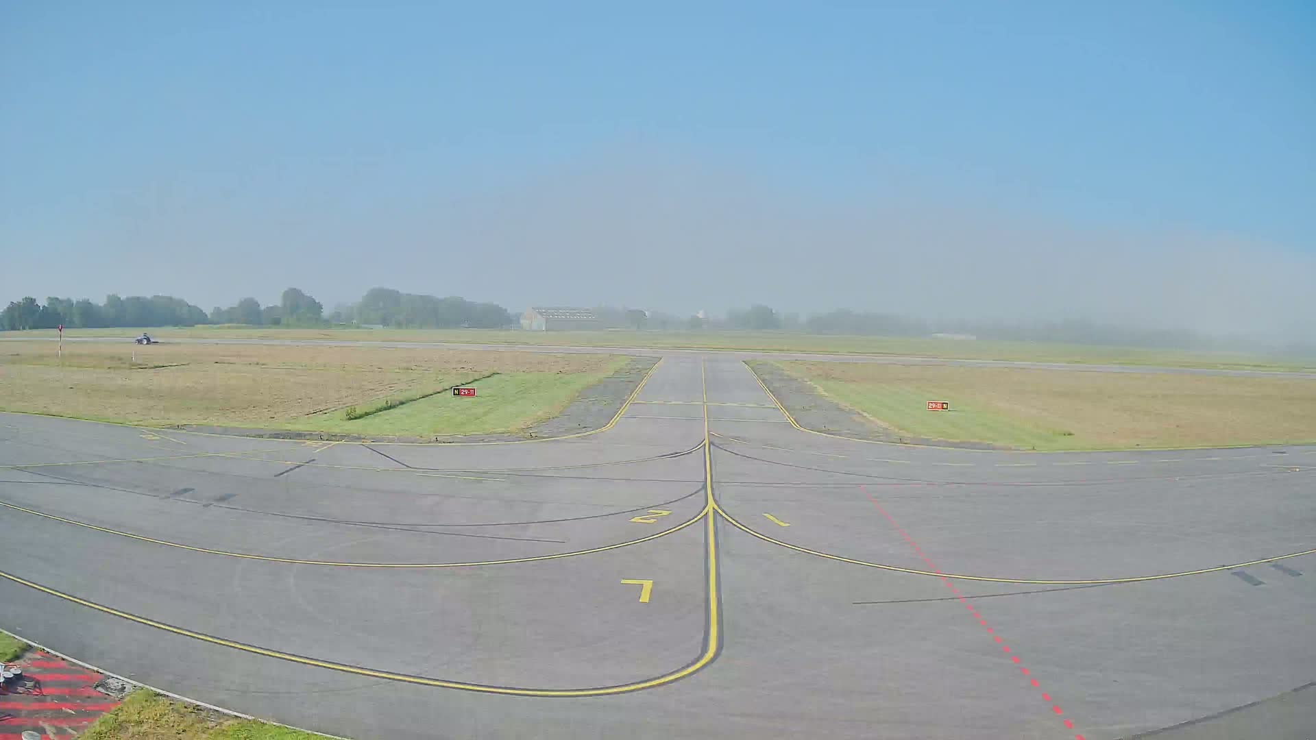A foggy airfield with a paved runway and taxiways is visible.