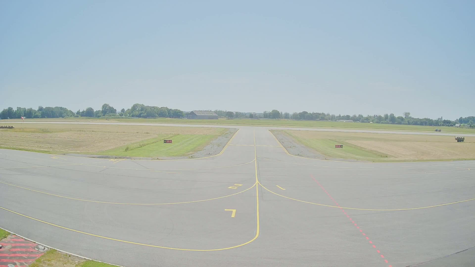 A runway at a small airport on a sunny day, with fields of cut hay visible beyond the tarmac.