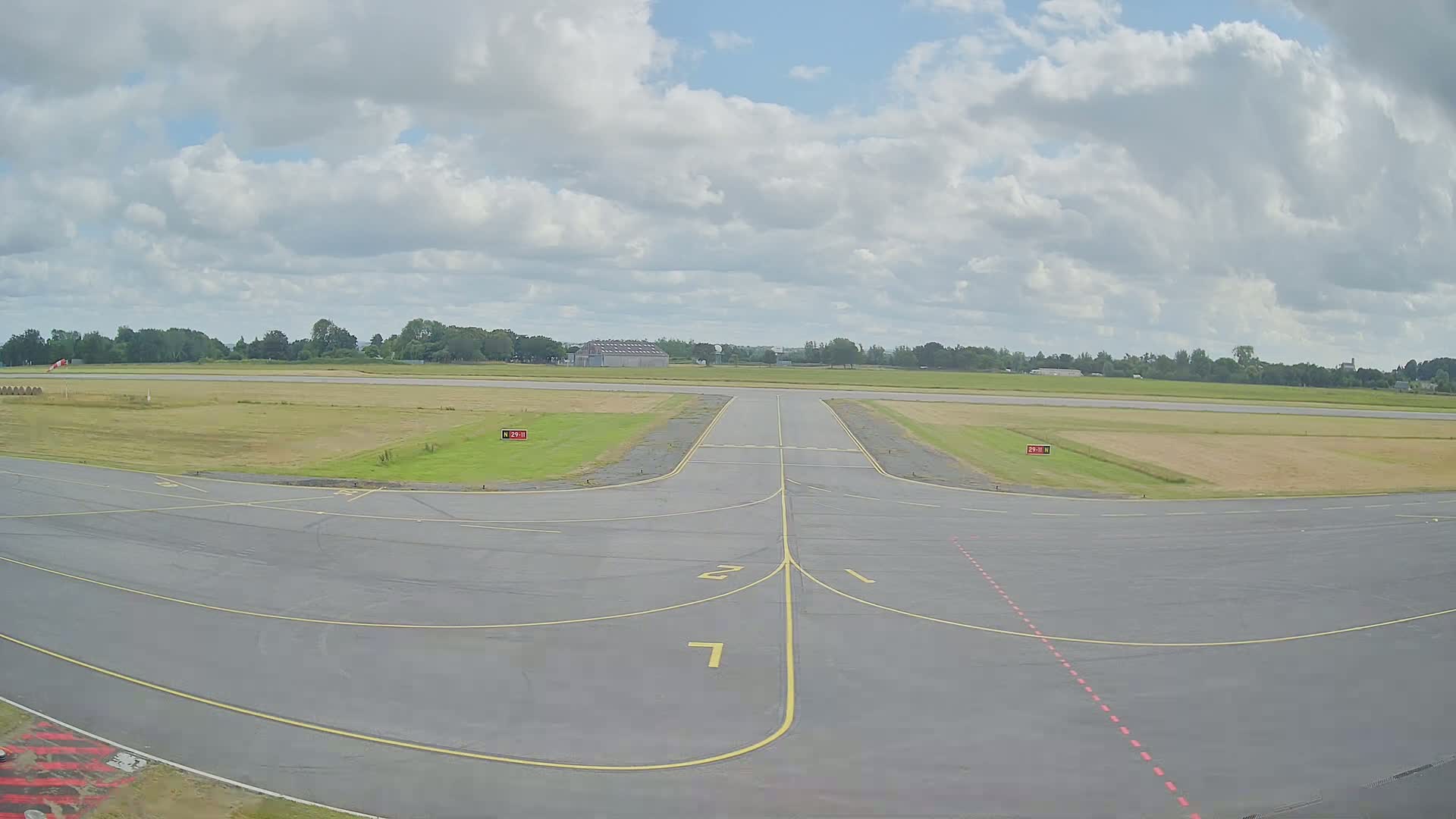 An airfield's taxiway and runway intersect under a partly cloudy sky.