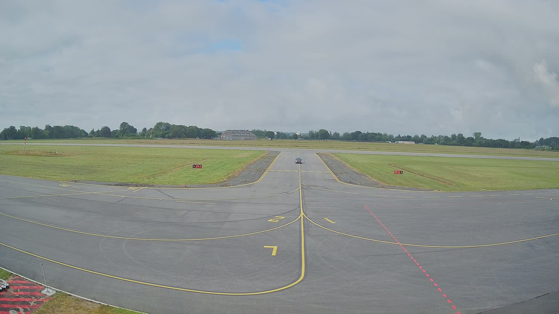 A vehicle drives down a runway at an airport on an overcast day.