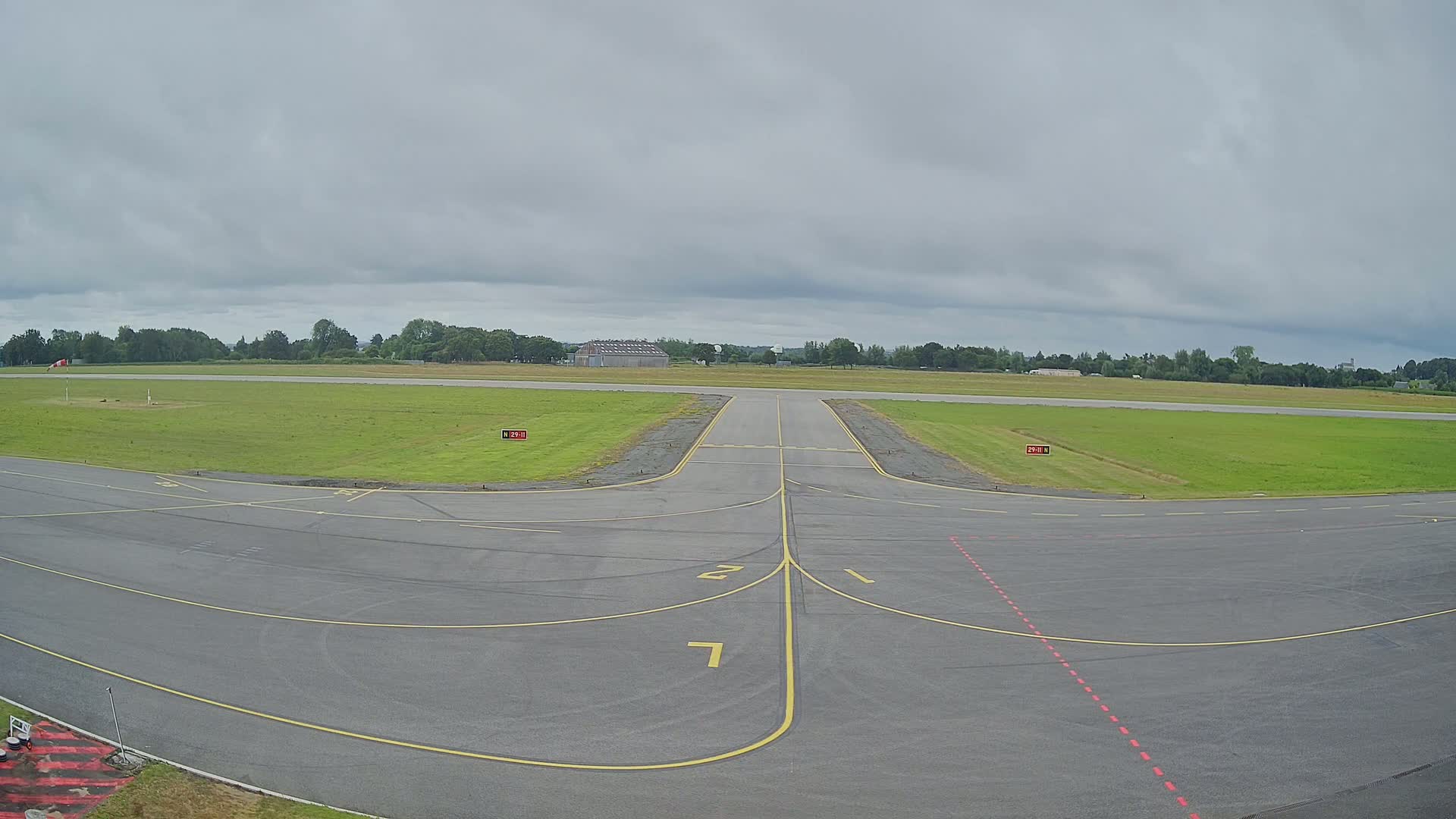A tarmac runway with yellow lines and a grassy airfield under an overcast sky.