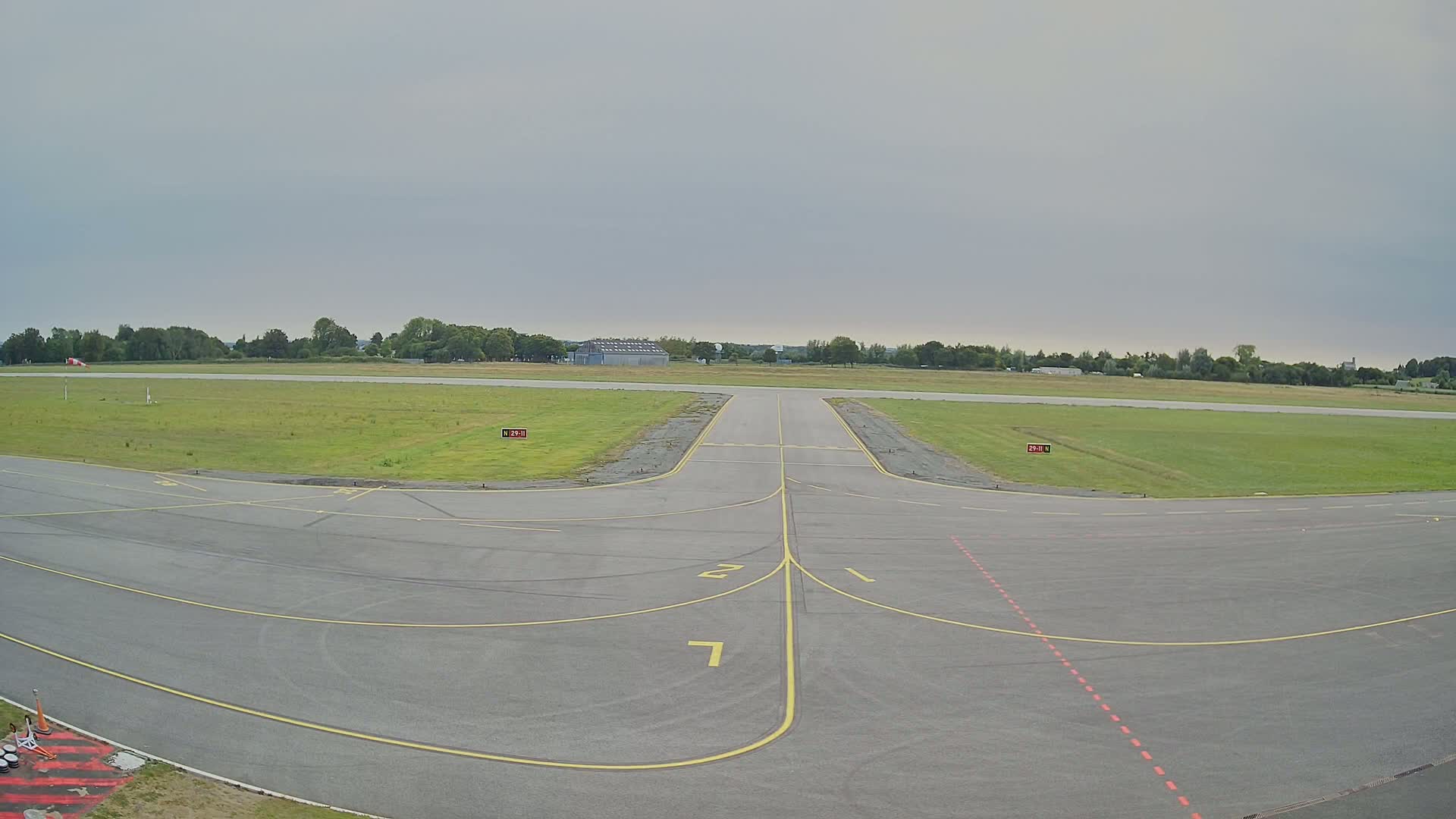 Under a bright moonlit night sky, a dark tarmac runway stretches into a field bordered by a treeline.