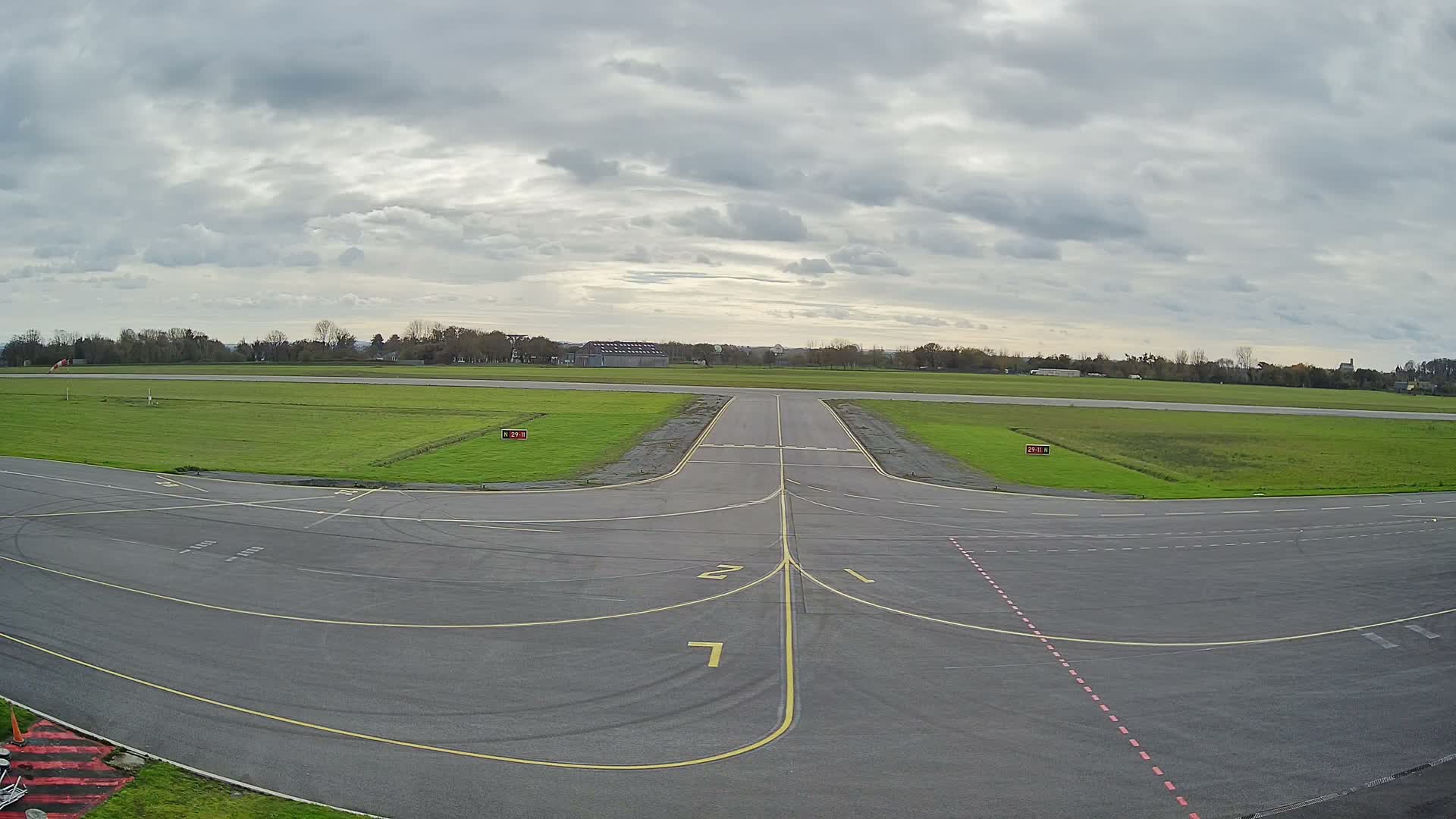 Under a bright moonlit night sky, a dark tarmac runway stretches into a field bordered by a treeline.